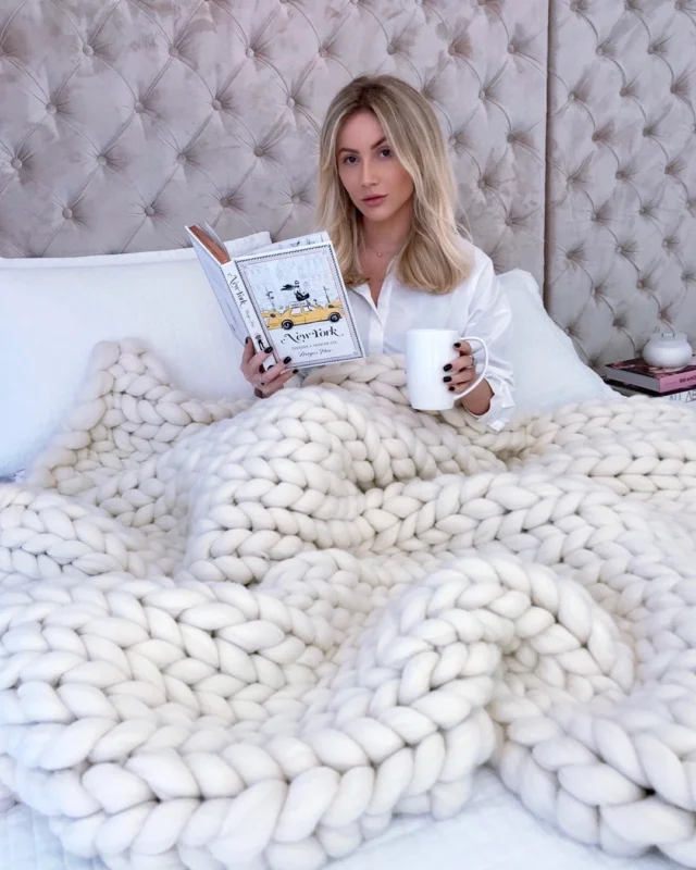 Mulher na cama com manta de maxi tricot feita com lã merino.