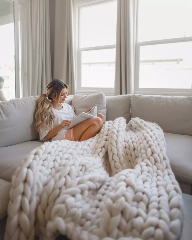 Mulher no sofá com uma manta de maxi tricot feita com lã merino.