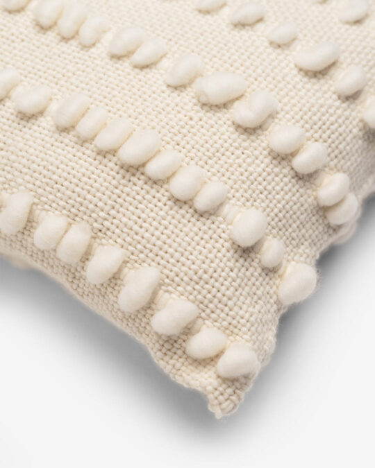 Detalhes do canto de uma almofada quadrada feita a mão em tear com lã merino cor cru natural.