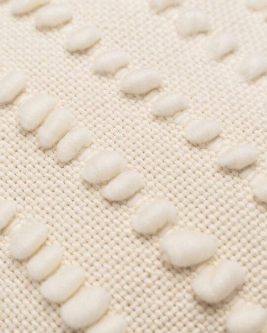 Detalhes da textura e tecido de uma almofada quadrada feita a mão em tear com lã merino cor cru natural.