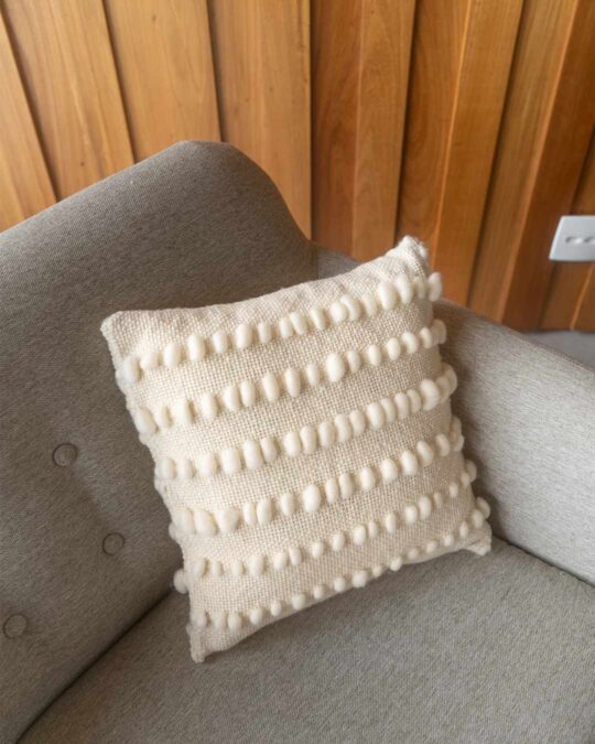 Poltrona decorada com almofada quadrada feita a mão em tear com lã merino cor cru natural.